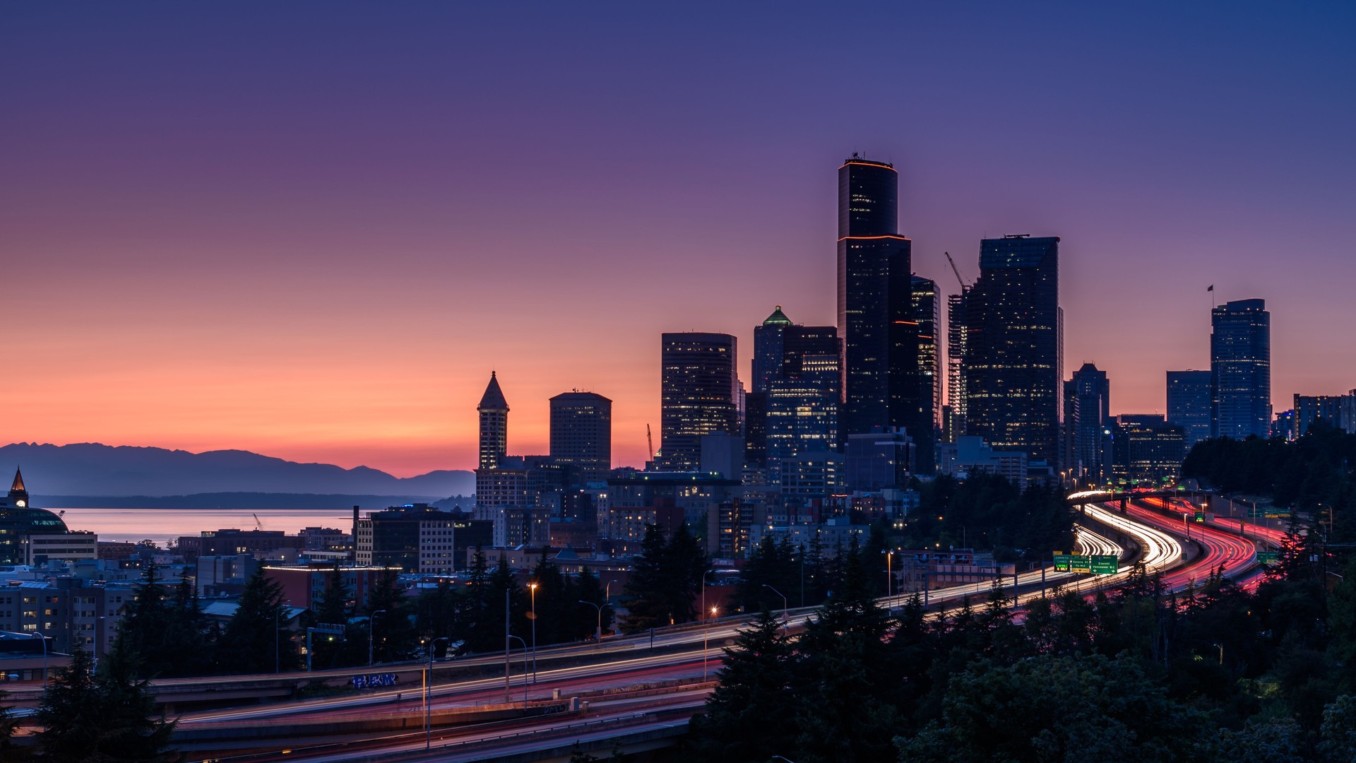 Seattle skyline, at sunset. The cars along the highway are creating light trails, due to a slow shutter speed